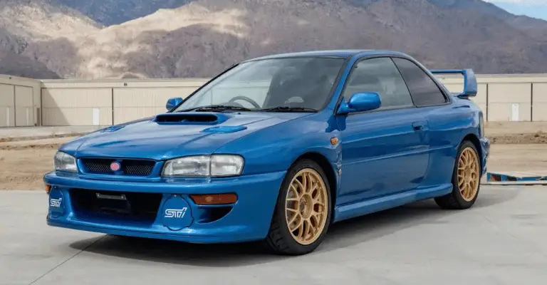 a blue and gold 22b subari impreza from the model year 2000. It's sitting against a mountain landscape with a road in the foreground.
